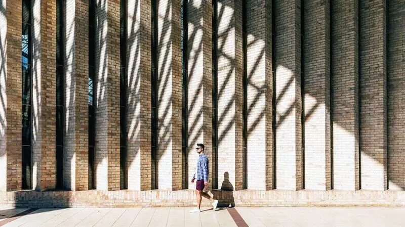A person walking by a brick wall on a sunny day.