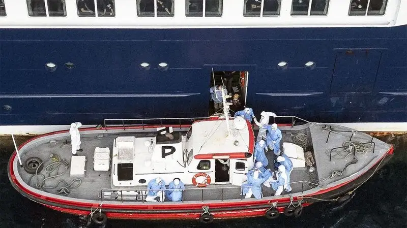 Health personnel in PPE assist hantavirus patients onto a boat