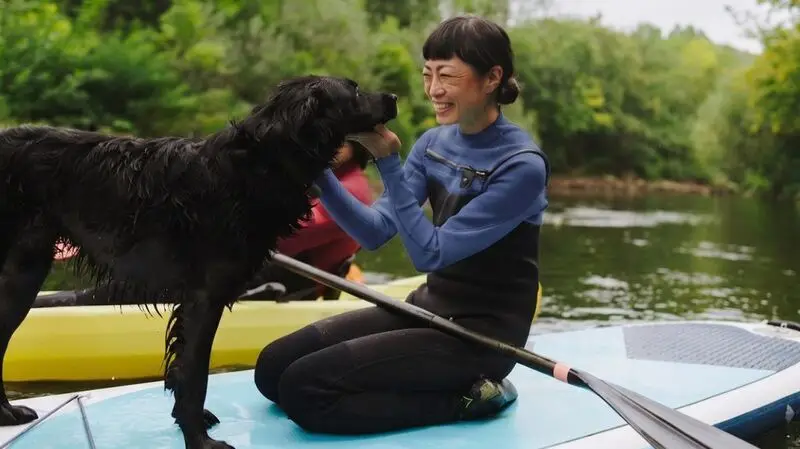 asian woman cuddling large black dog on kayak