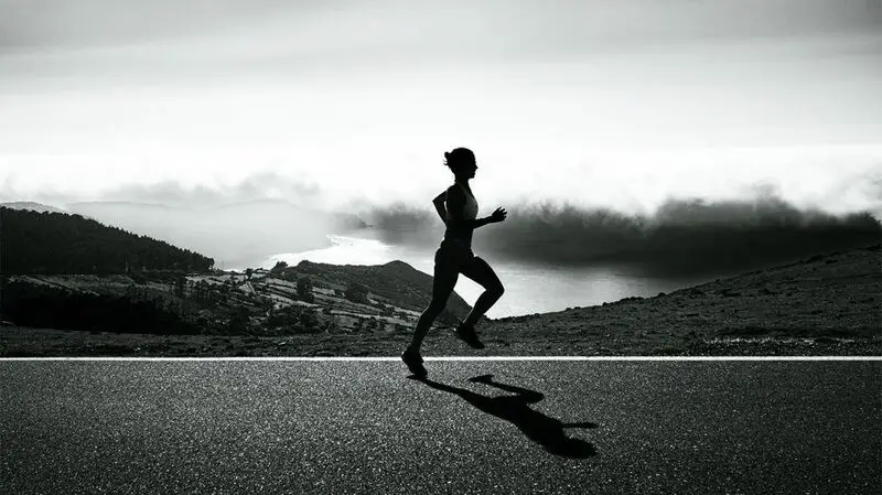 Silhouette of runner on mountain road with dramatic landscape.