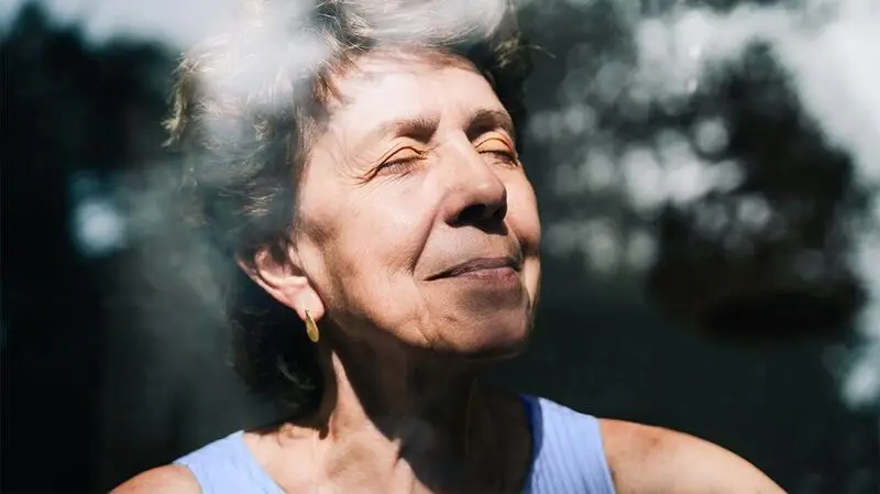 portrait of older white woman with her eyes closed by a window