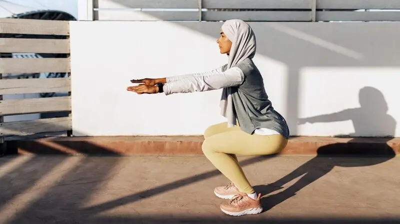A person wearing athletic gear and a hijab does pilates outdoors in sunlight