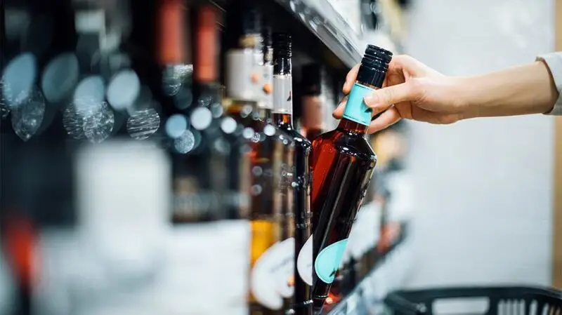 A person reaches for a bottle of alcohol on a shelf in a supermarket