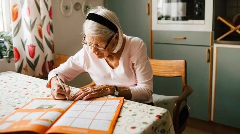 older white woman solving crosswords at the kitchen table