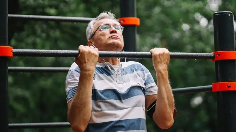 An older man does a chin up on a bar to exercise