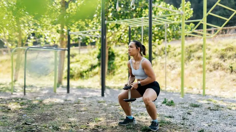 A female squatting with a dumbbell.