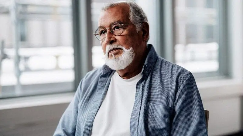 An older male adult speaks to a healthcare provider in a room, only the patient visible